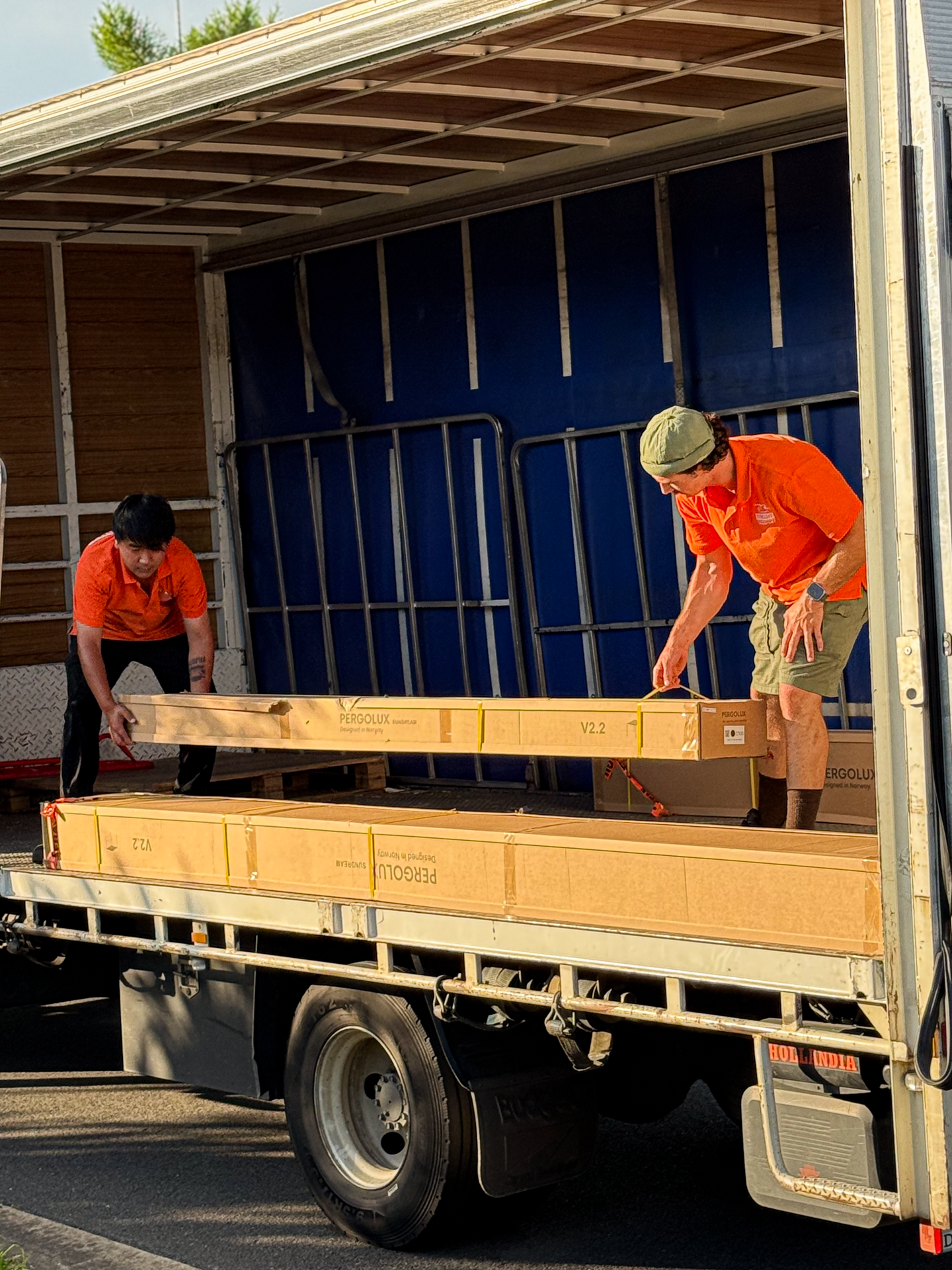 Two men in orange shirts loading a large wooden board into a truck.