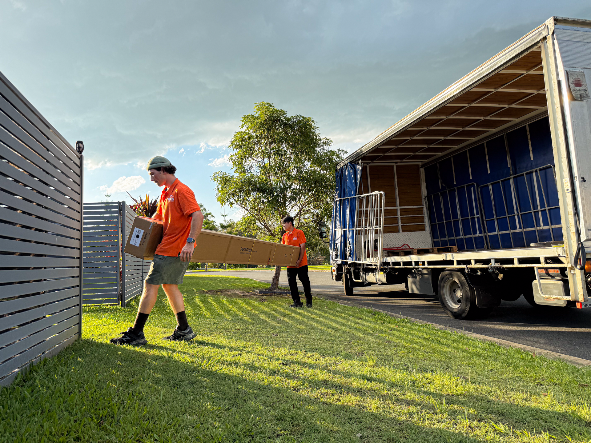 Two men with delivery parcel near a truck on a grassy area.