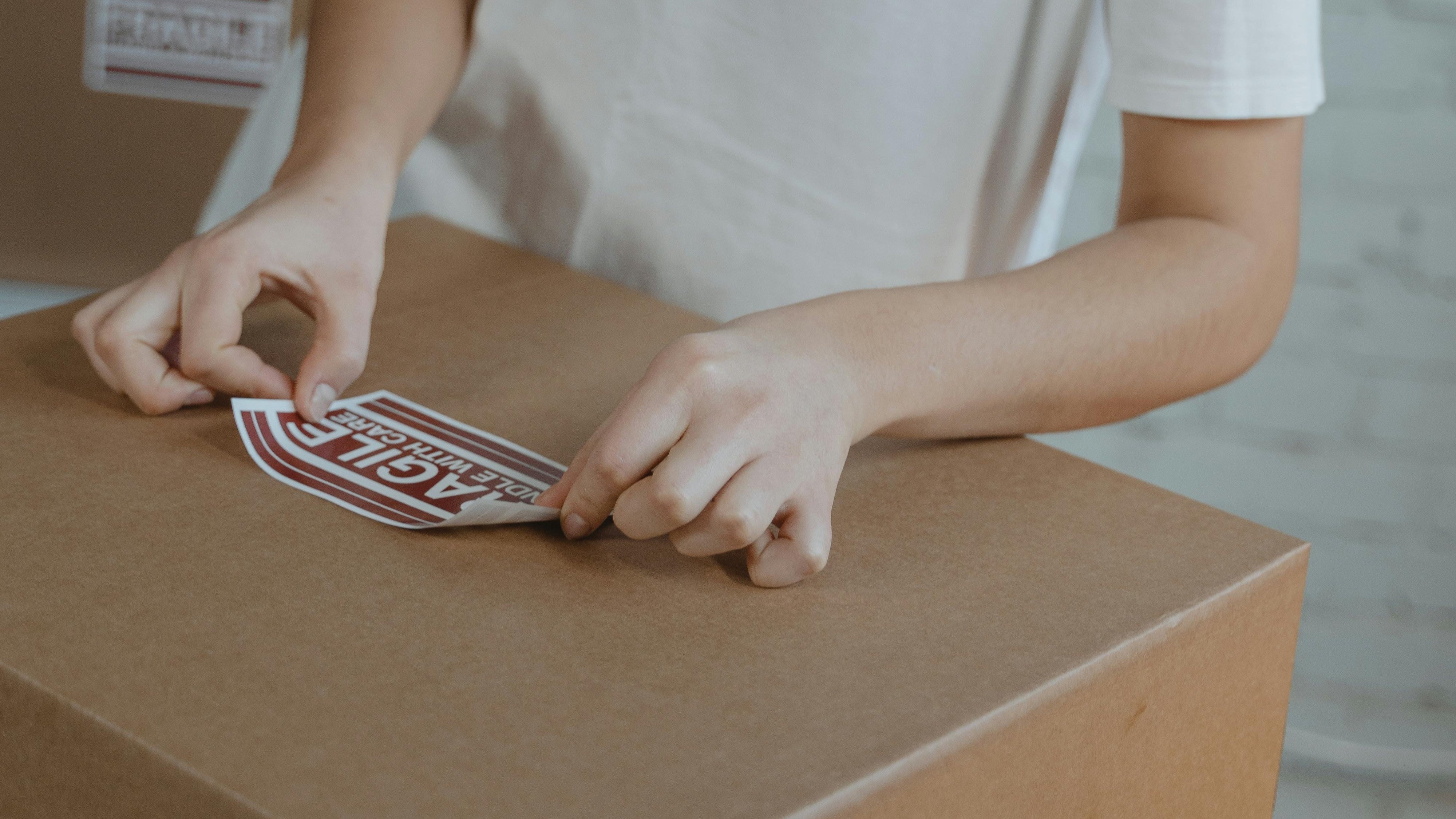 Person applying a label to a cardboard box in a warehouse setting
