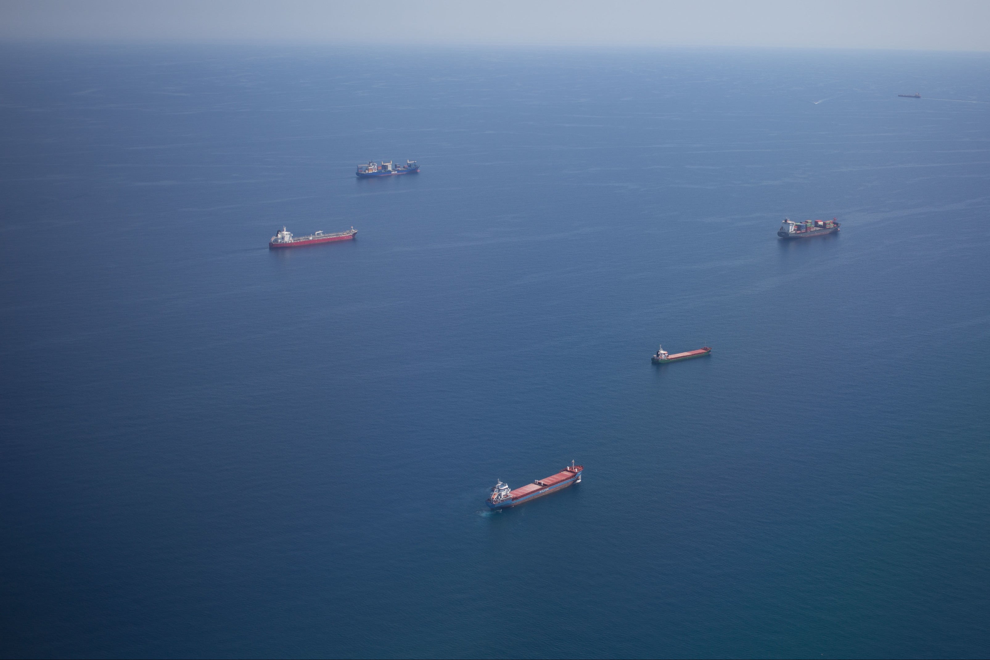 Aerial view of cargo ships on a clear day with an airplane wing in the foreground.