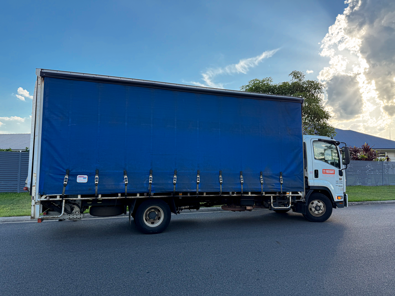 Blue truck with a curtain side on a road under a blue sky with clouds.